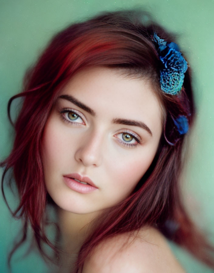 Red-haired woman with green eyes and blue floral accessory on soft green backdrop