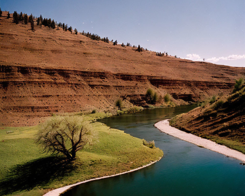 Tranquil river winding through lush green landscape with tree, red-rock cliffs, and blue sky