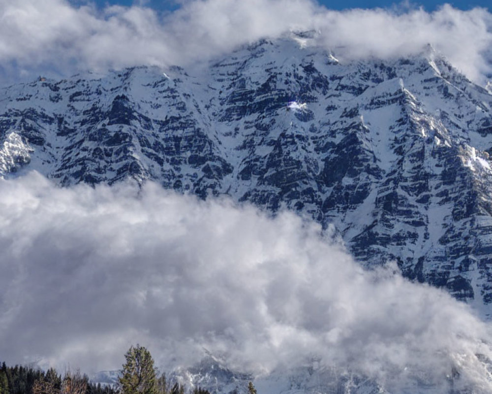 Majestic snow-covered mountain peaks above clouds and forest landscape