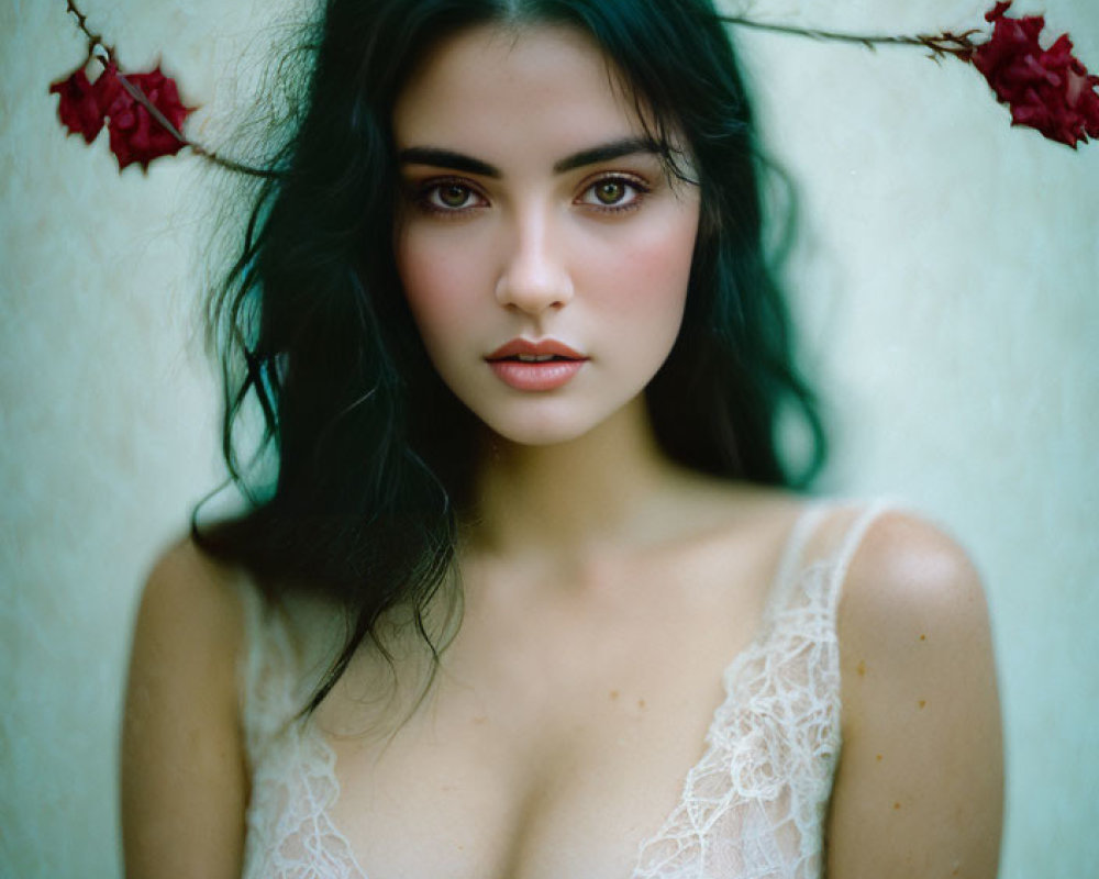 Dark-haired woman with striking eyes surrounded by red flowers in white lace attire.