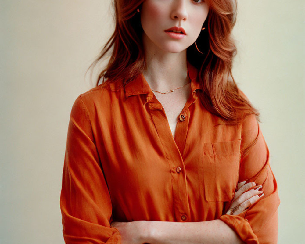 Red-haired person in orange shirt and blue jeans with crossed arms.