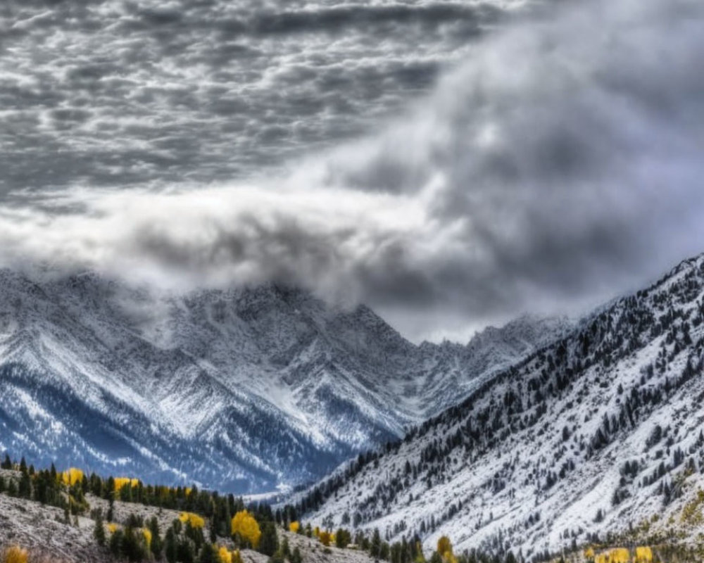 Snow-covered mountains under dramatic cloudy sky with autumn foliage.