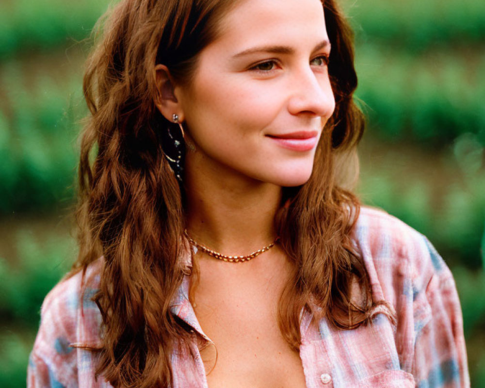 Long-haired woman in plaid shirt and overalls smiling in green field