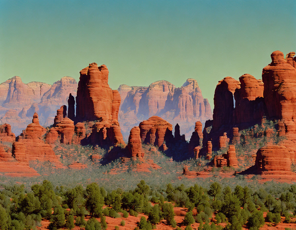 Red Sandstone Rock Formations Amidst Green Shrubs on Clear Blue Sky