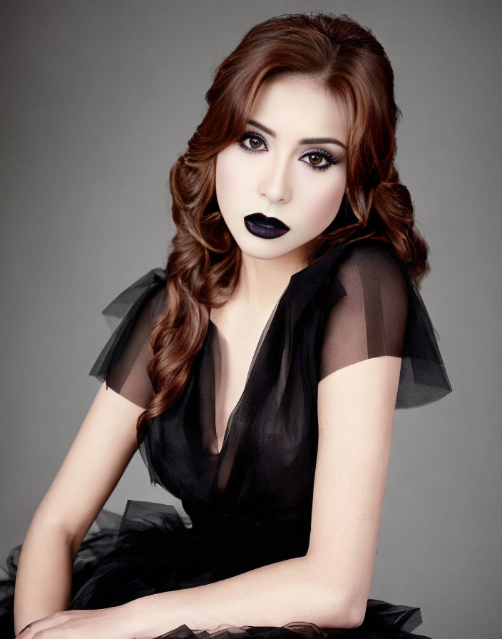 Woman with wavy hair in black dress against gray backdrop