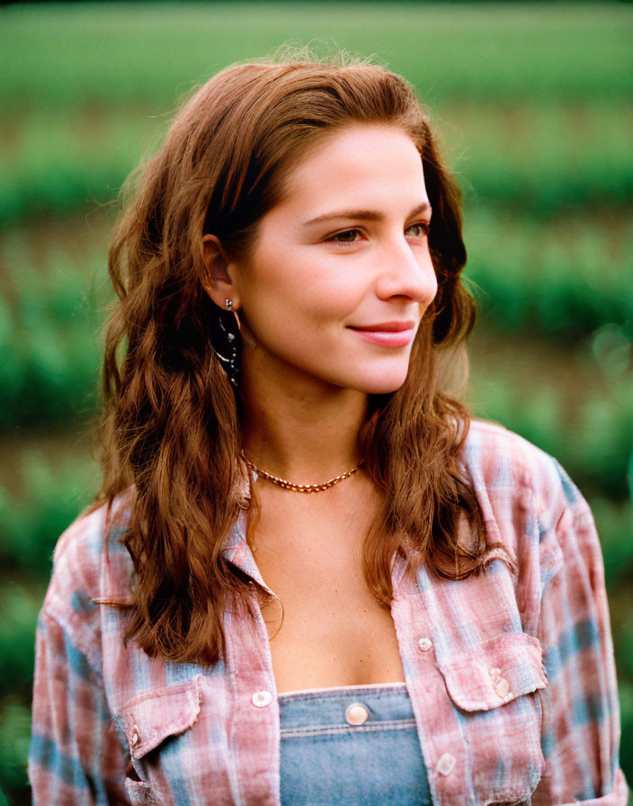 Long-haired woman in plaid shirt and overalls smiling in green field