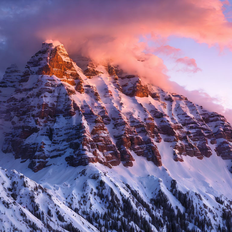 Majestic snow-covered mountain peak at sunset with vibrant orange clouds and alpenglow.