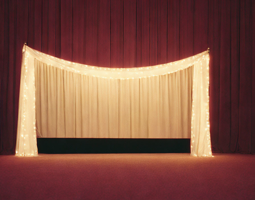 Closed theater stage with cream curtain and fairy lights on red backdrop.