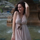 Woman in flowing dress by water's edge with blossoming foliage background