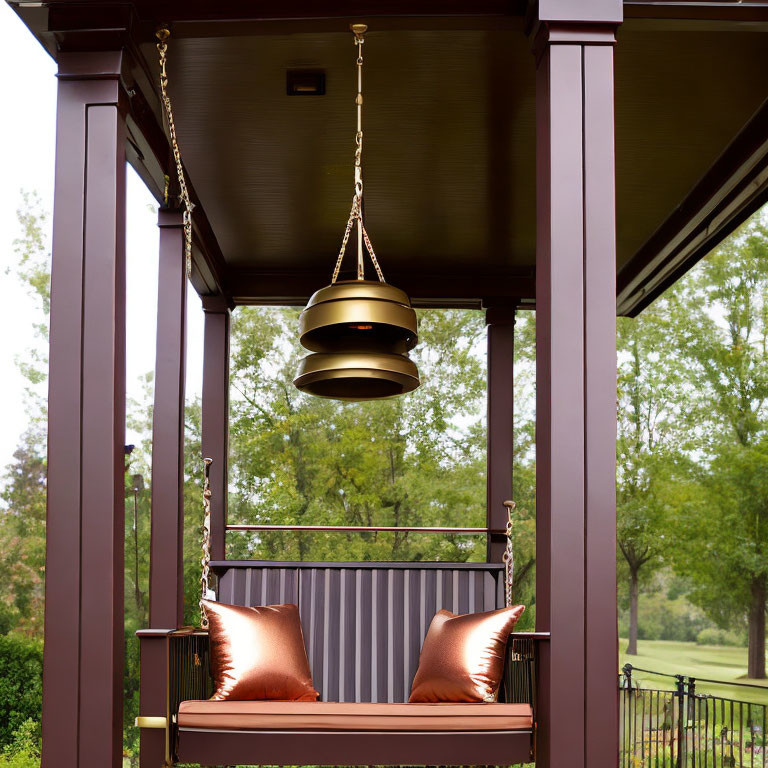 Cozy porch with swing bench, orange pillows, and brass light fixture overlooking grassy area