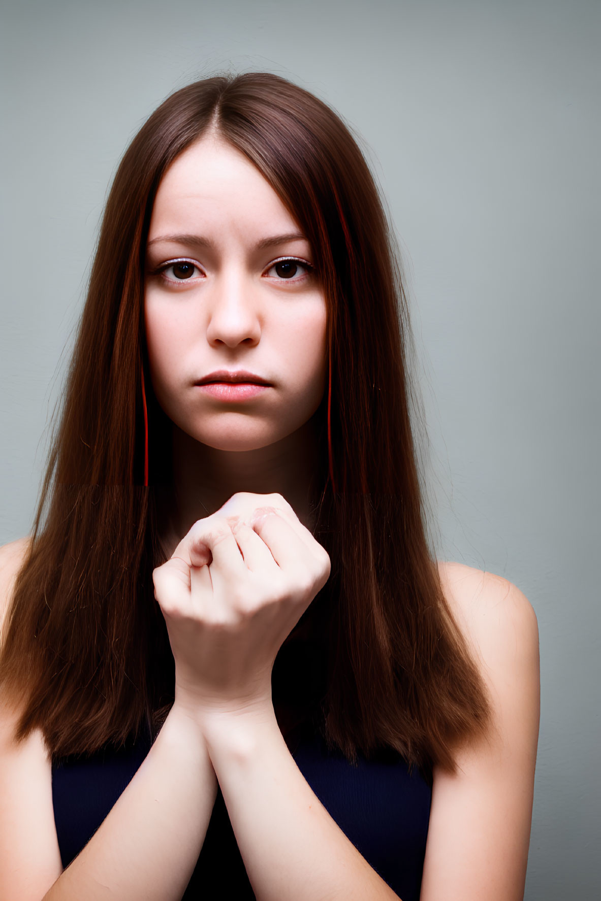 Young woman with brown hair in dark top and red earrings on gray background.