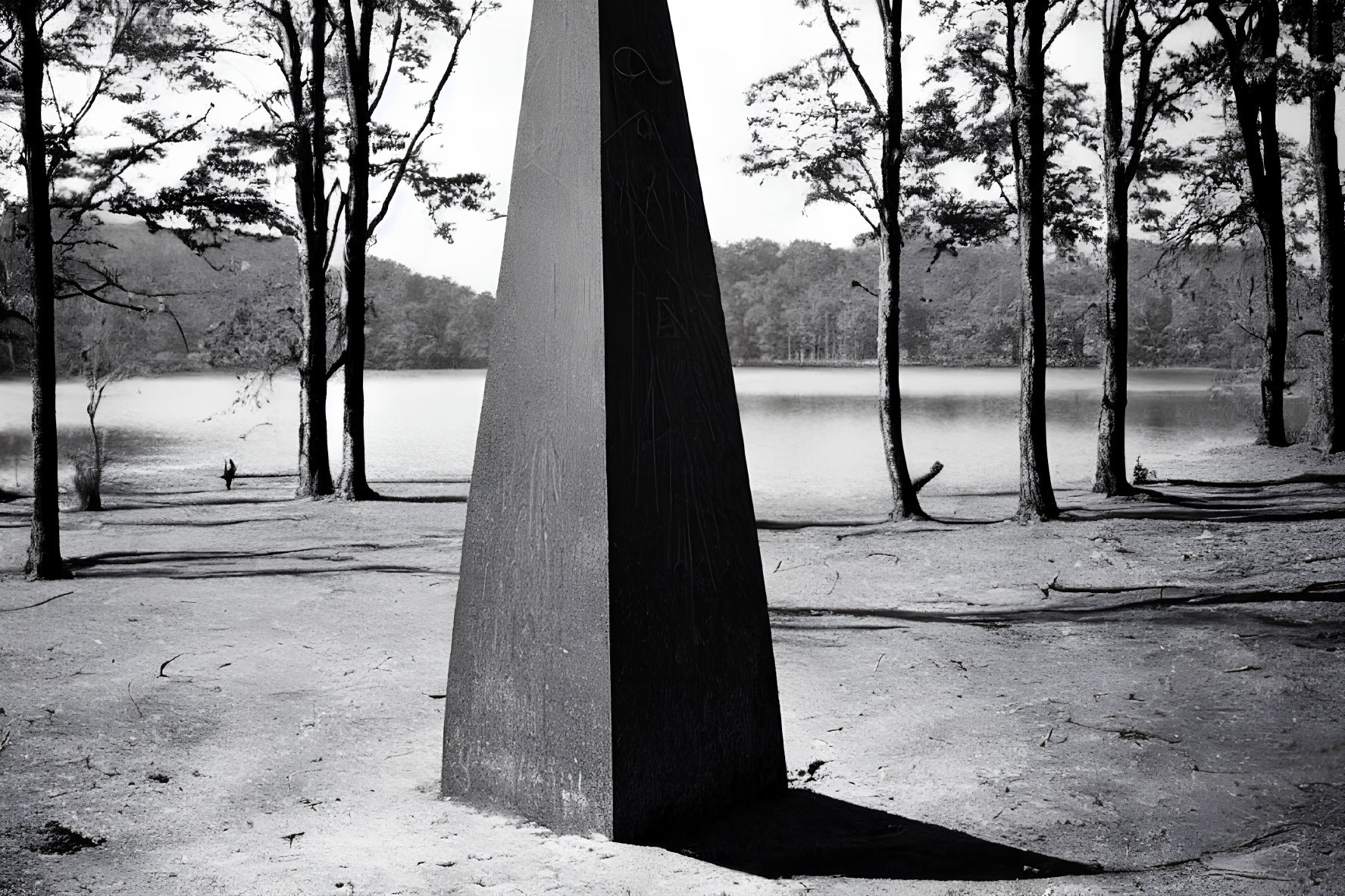 Monochrome image of triangular sculpture in forest with lake view