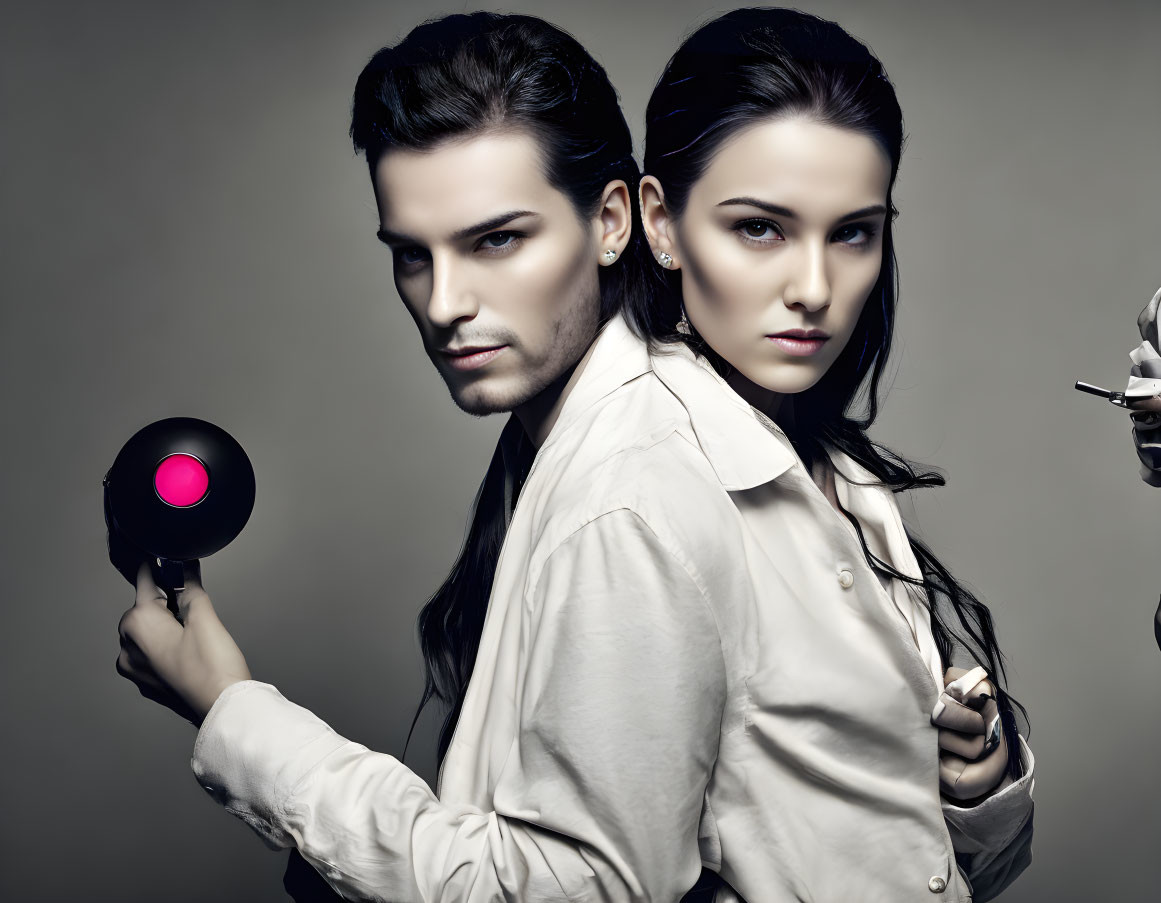 Fashionable man and woman with sleek hairstyles pose back-to-back with a hairdryer.