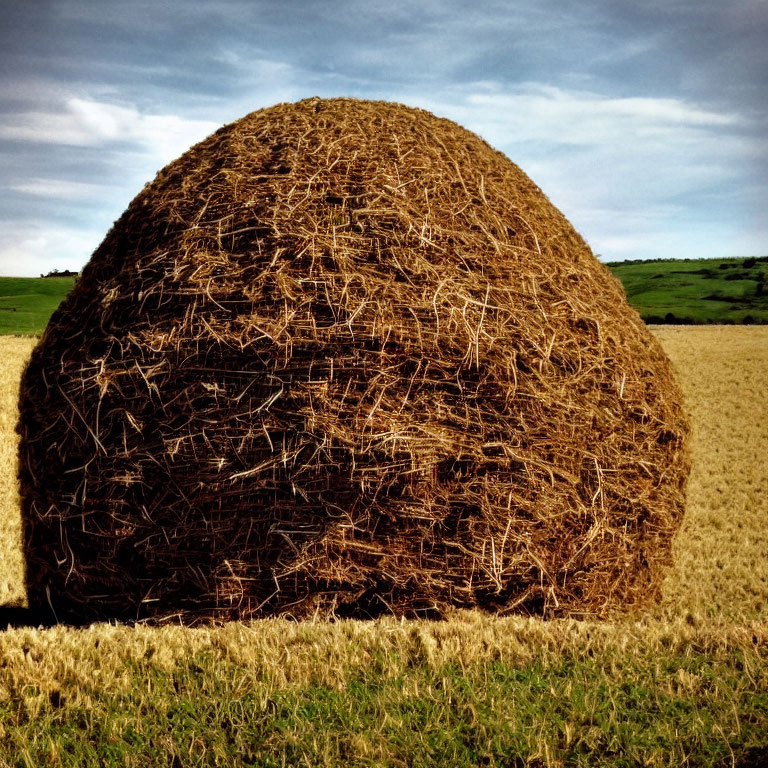 Large haystack in field under cloudy blue sky