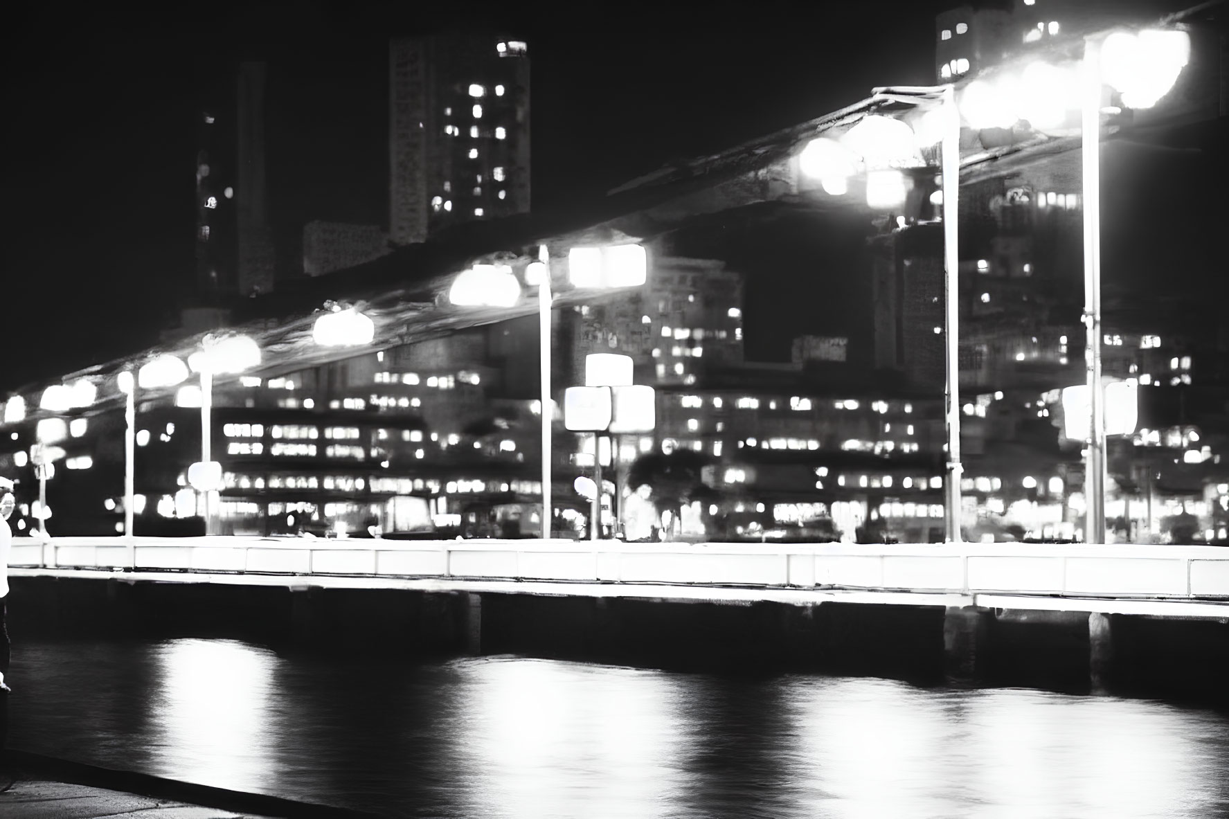 Monochrome cityscape at night with waterfront streetlights and blurred reflections