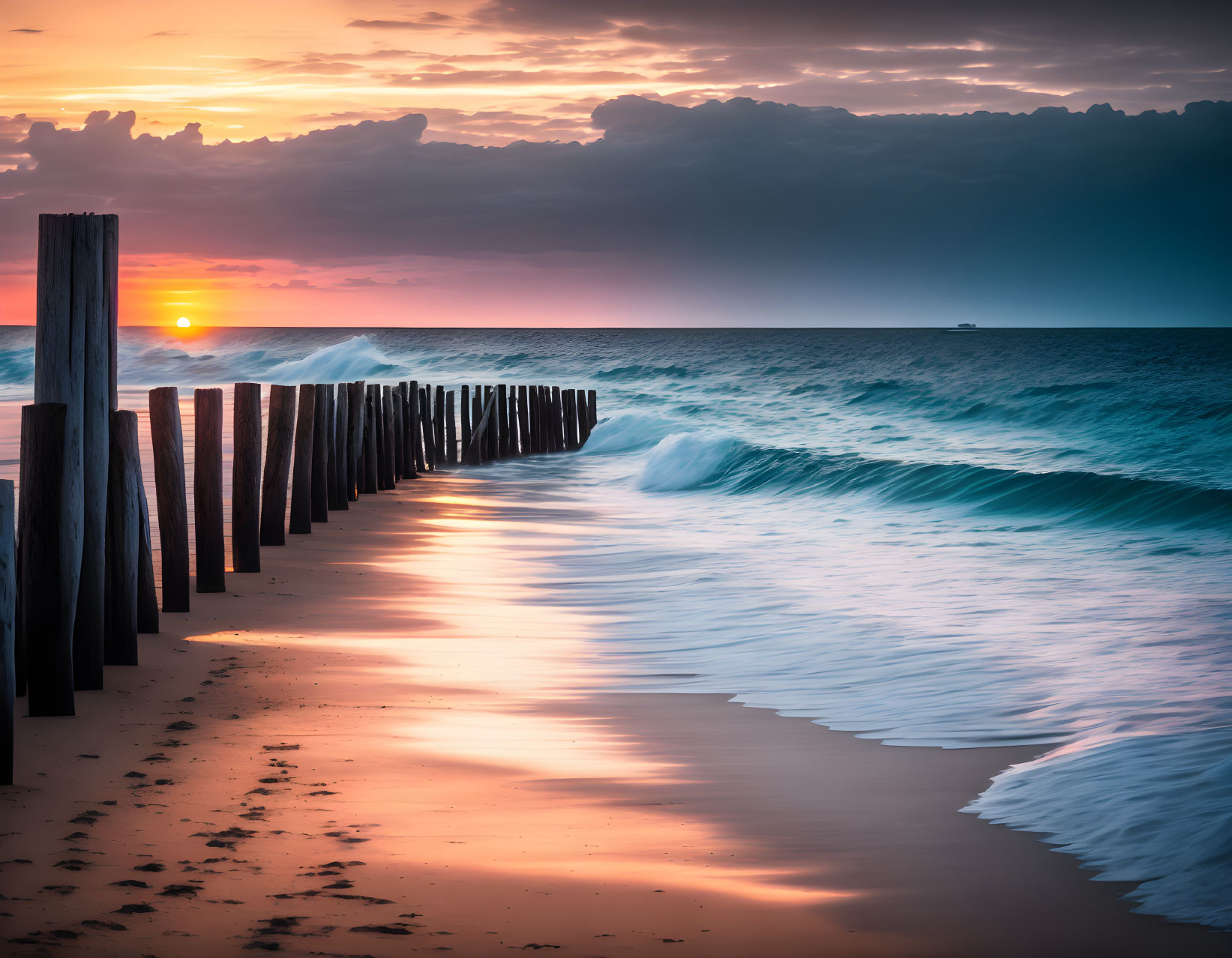 Dramatic sunset beach scene with wooden posts, crashing waves, and distant ship.