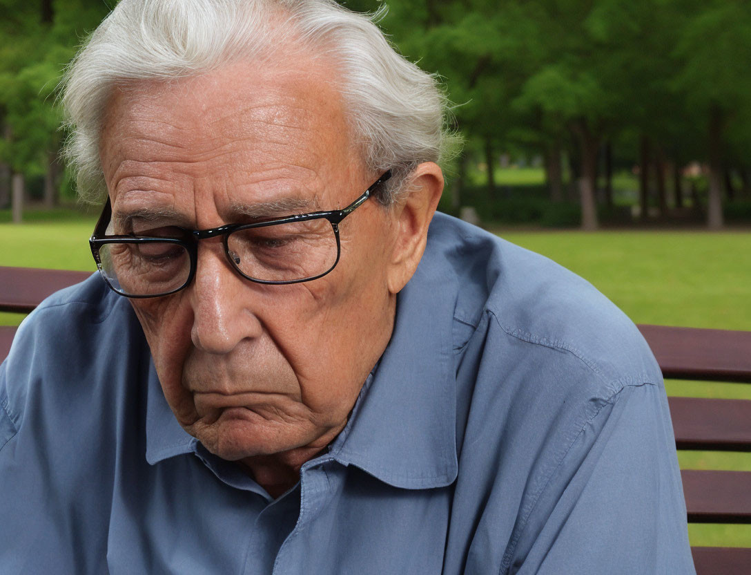 Elderly man in blue shirt sitting on park bench with trees in background