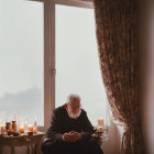 Elderly bearded man sitting by window with candles and misty landscape