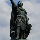 Black-clad Figure Statue with Helmet, Wire, and Gears Against Cloudy Sky