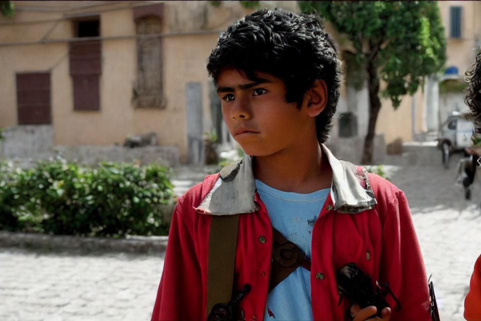 Young boy in red jacket on sunlit cobblestone street