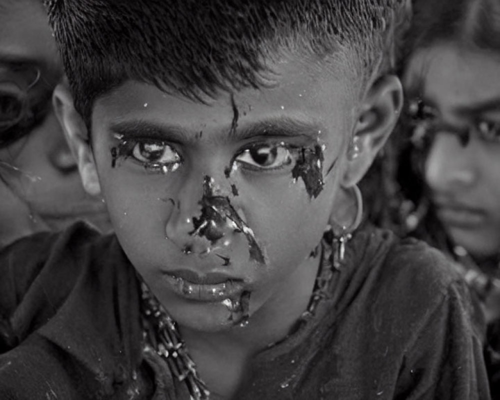 Monochrome image of child with solemn expression and dark smudges, surrounded by other faces.