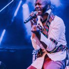 Male performer in cream jacket and bow tie singing on blue-lit stage