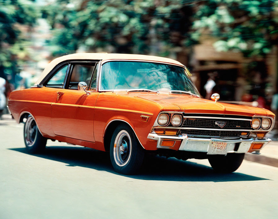 Vintage orange car with chrome grille and white-wall tires parked on street