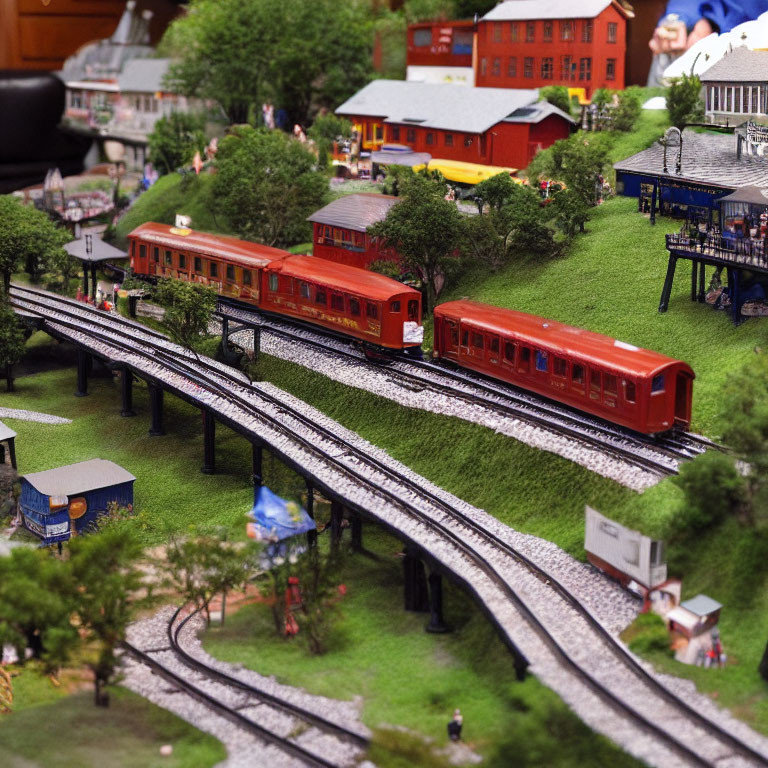 Detailed miniature model train set with red carriages crossing landscape, tiny buildings, trees, and figurines