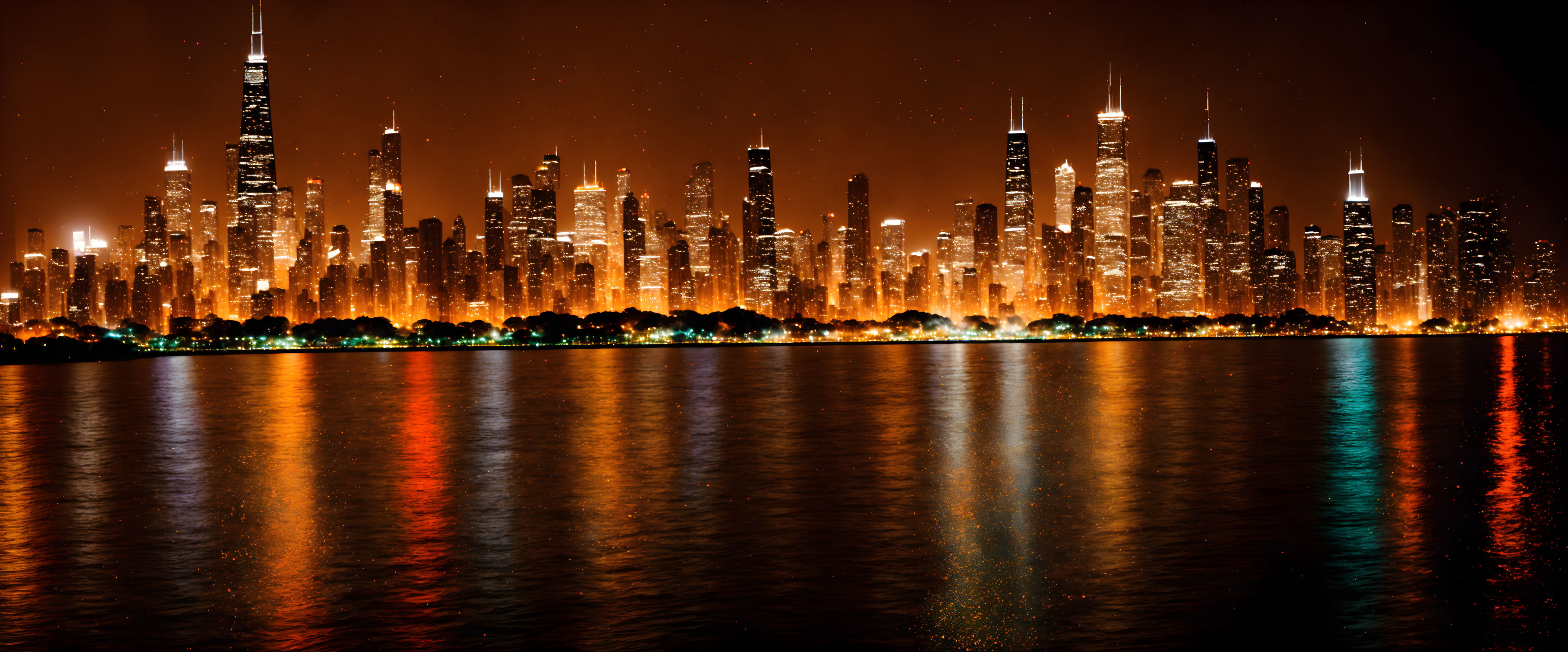 Panoramic nighttime cityscape with illuminated skyscrapers reflected on calm waterfront