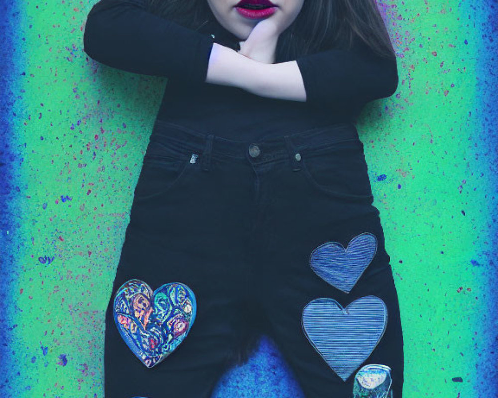 Dark-haired woman with bold makeup poses in black outfit with heart patches against colorful backdrop