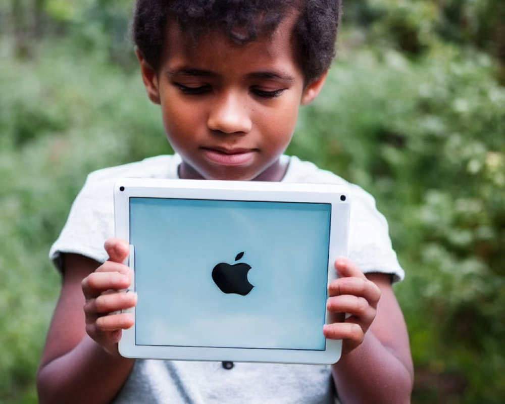 Child with Apple logo tablet in green garden