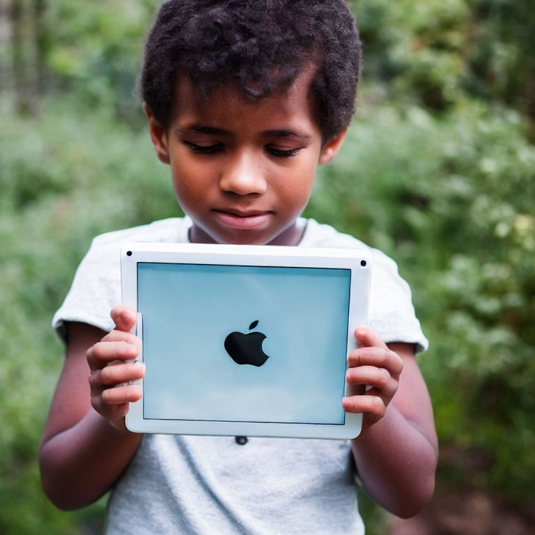 Child with Apple logo tablet in green garden