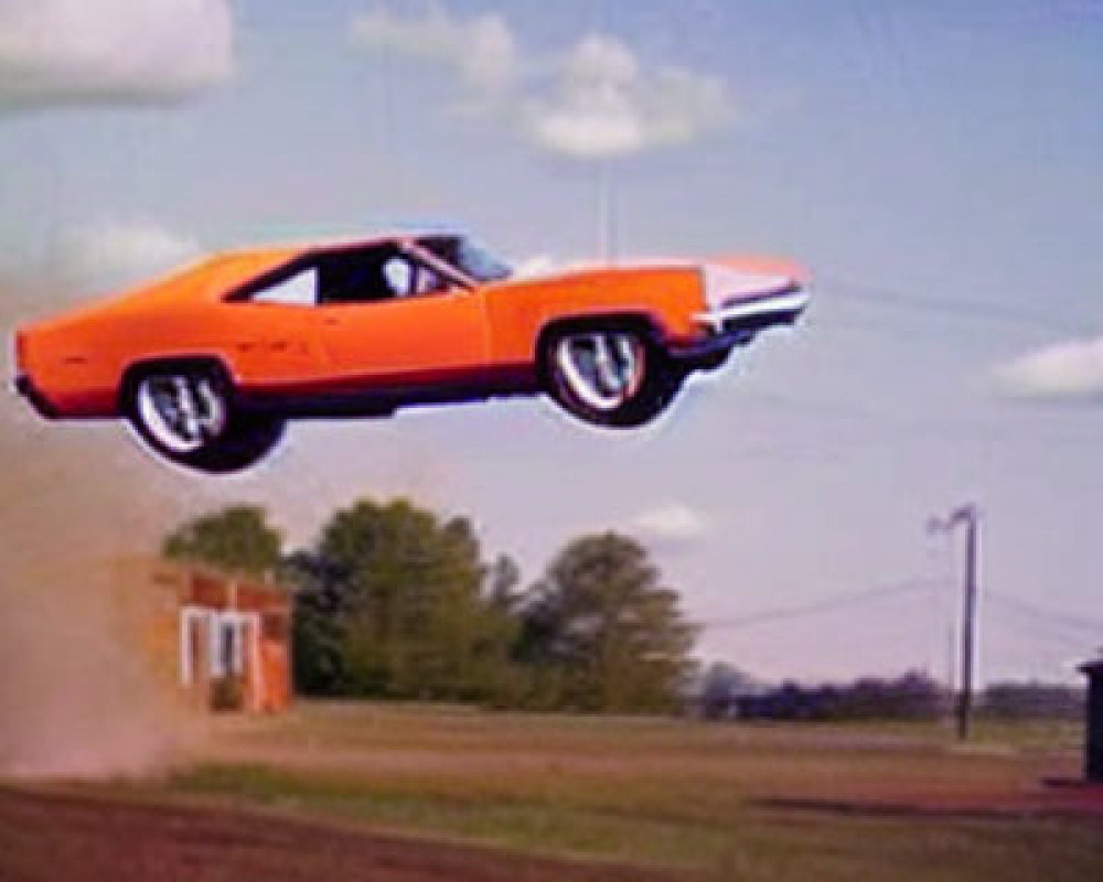 Bright Orange Muscle Car Mid-Air Against Blue Sky