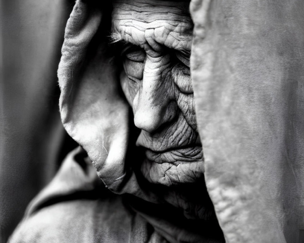 Monochrome portrait of elderly person in hooded cloak, emanating wisdom.