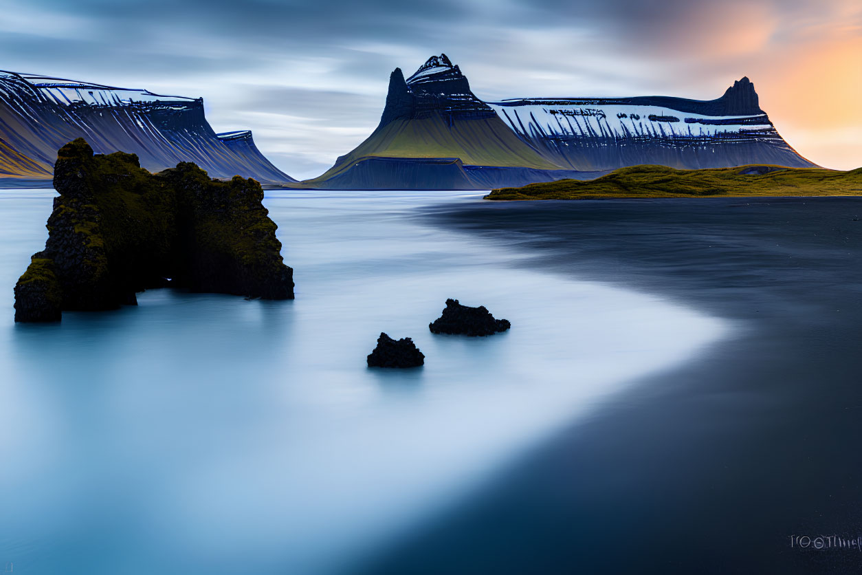 Tranquil landscape with reflective blue water, sandy shore, and layered mountains