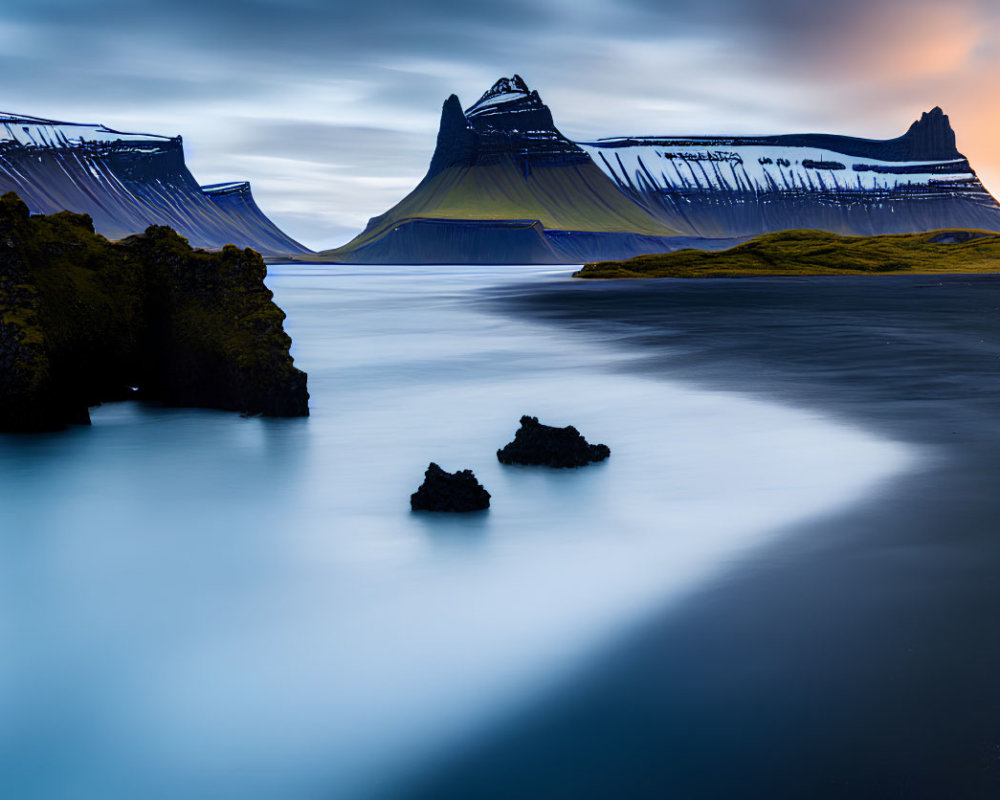 Tranquil landscape with reflective blue water, sandy shore, and layered mountains