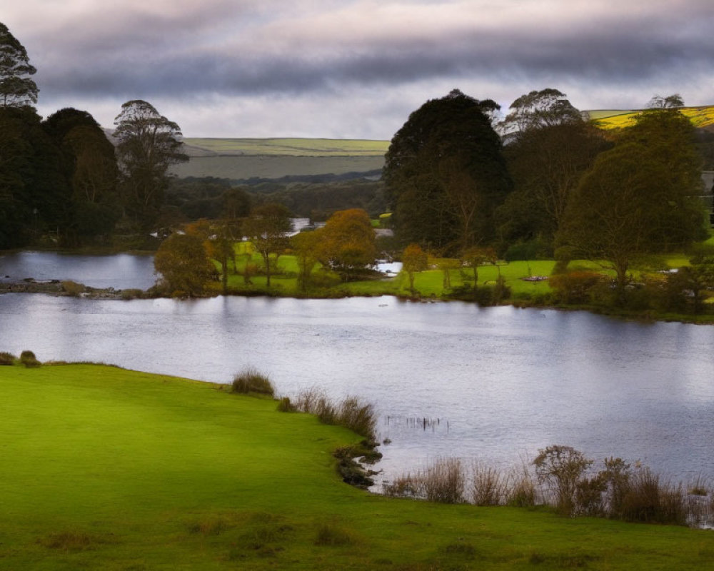 Tranquil lake surrounded by green hills and autumn trees under dramatic sky