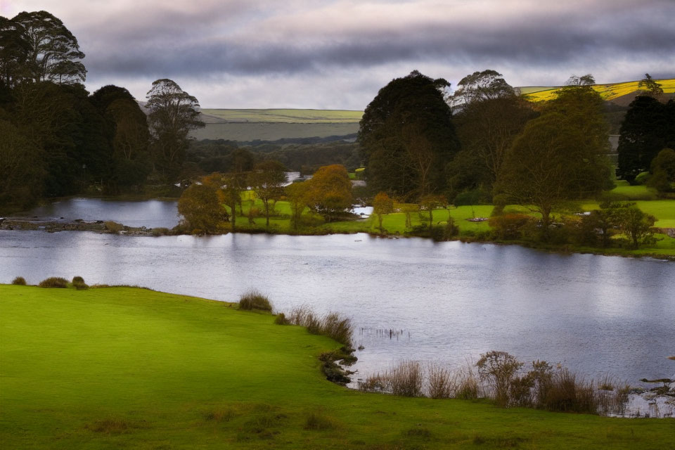 Tranquil lake surrounded by green hills and autumn trees under dramatic sky