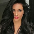 Woman in Blue and Brown Feather Headdress with Red Lips and Thoughtful Expression against Natural Background