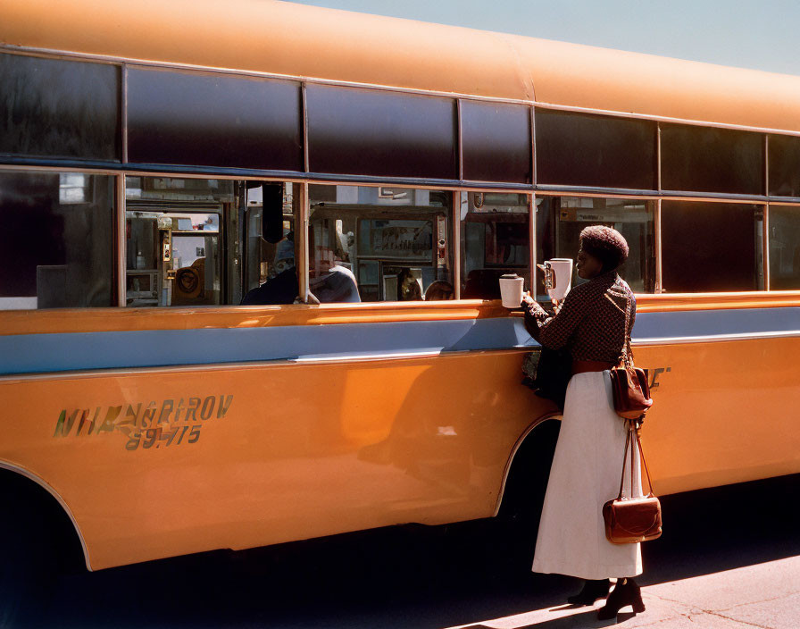 Person reading by yellow bus with driver inside, clear sky