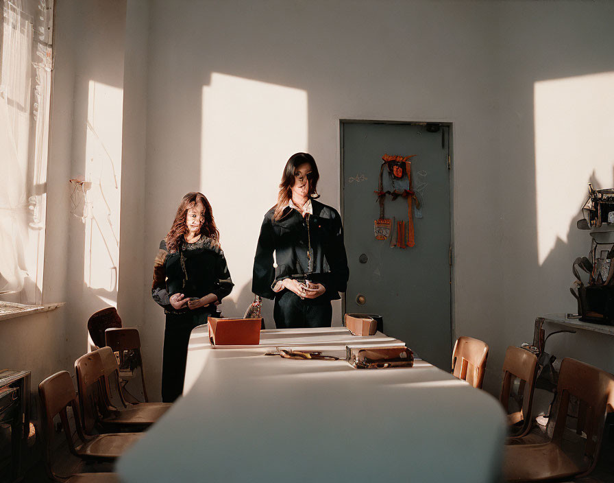 Two women at table in sunlit room with book and decorative item.