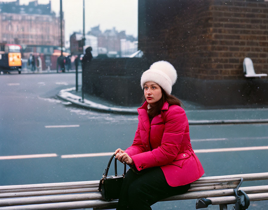 Woman in Pink Coat and White Hat Sitting on City Guardrail with Blurred Urban Background