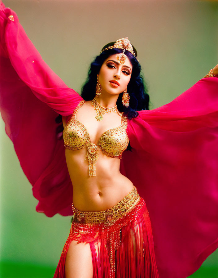 Woman in golden belly dancing costume with pink veil on green background