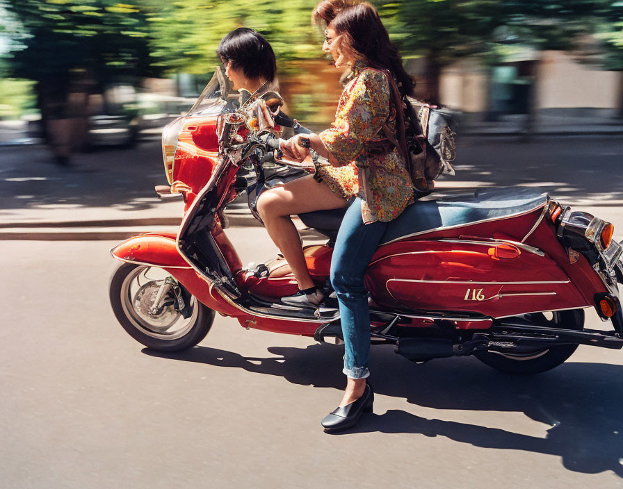 Two people on red scooter under sunny sky with blurred trees in background