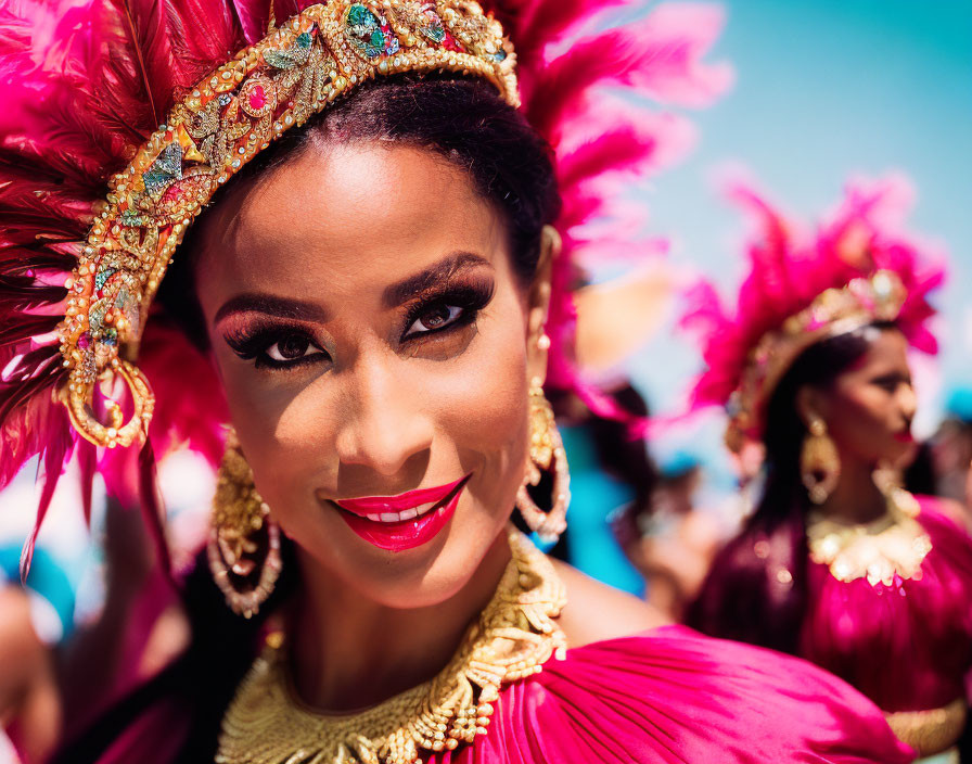 Woman in vibrant red feather headwear and gold jewelry smiling at festive event with blurred background.