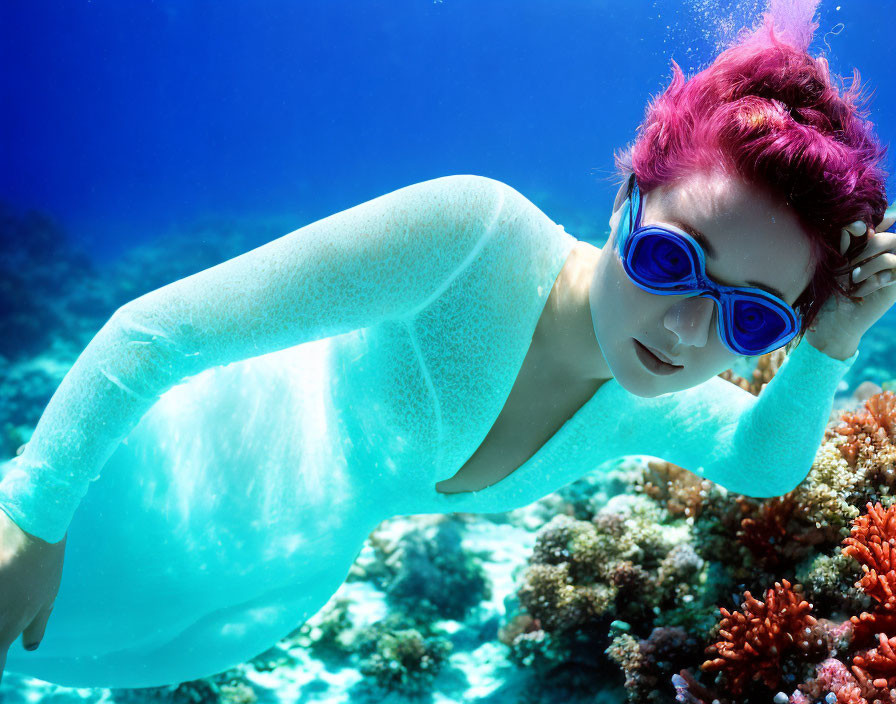 Person with Pink Hair and Blue Goggles Swimming by Vibrant Coral Reefs