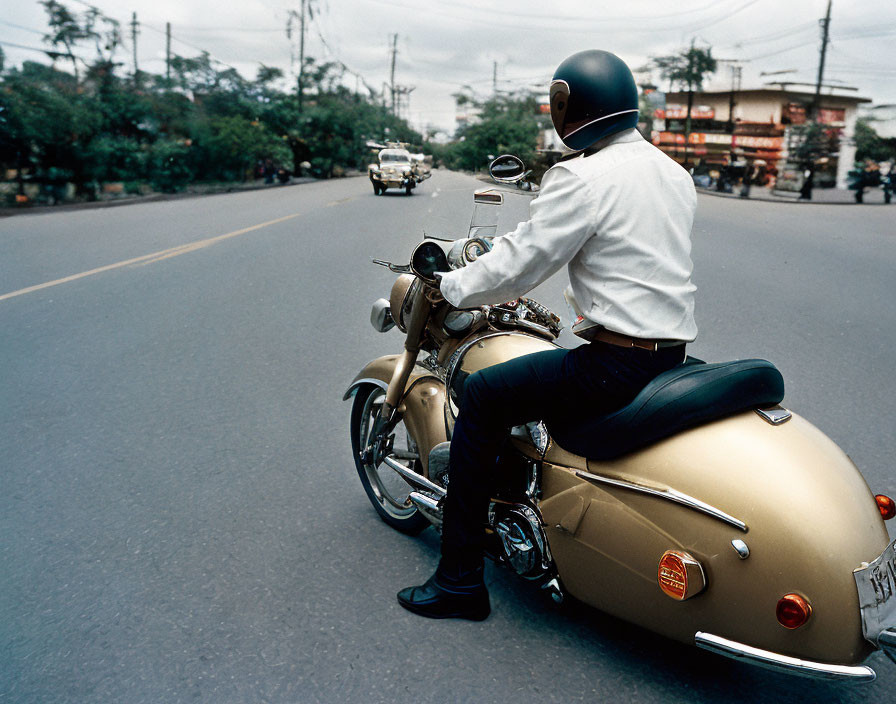 Person in White Shirt and Helmet Riding Classic Motorcycle on Urban Road