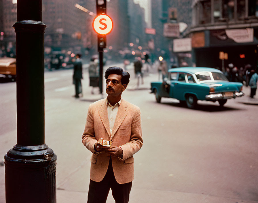 Man in Tan Jacket and Dark Glasses with Camera by Red "S" Sign and Vintage Cars