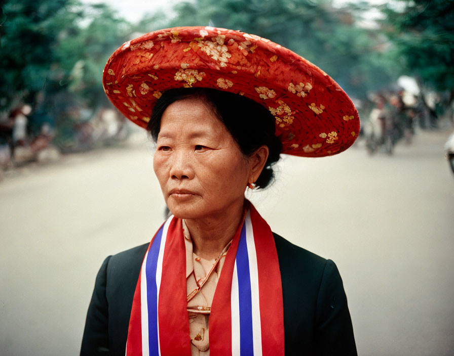 Woman in Red Floral Hat with Sash Against Street Background