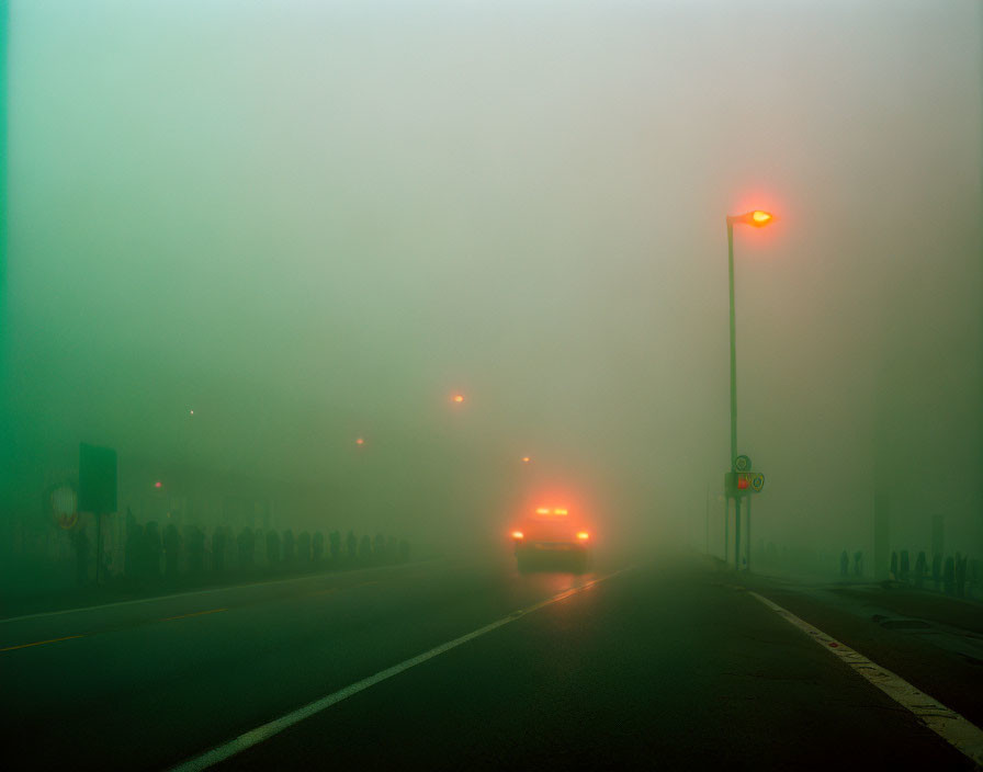 Vehicle with illuminated taillights on foggy road under dim orange streetlights